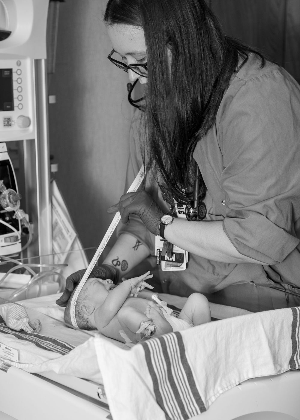 Black and white photo of a nurse caring for a newborn baby in a NICU, with medical equipment visible nearby.