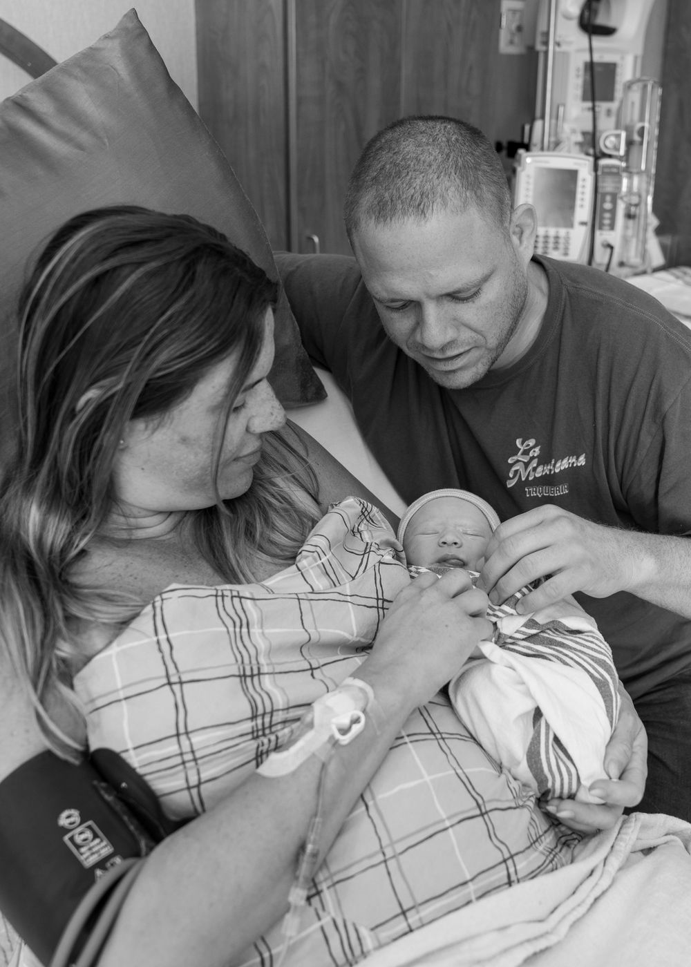Black and white photo of new parents in hospital room lovingly gazing at their newborn baby.