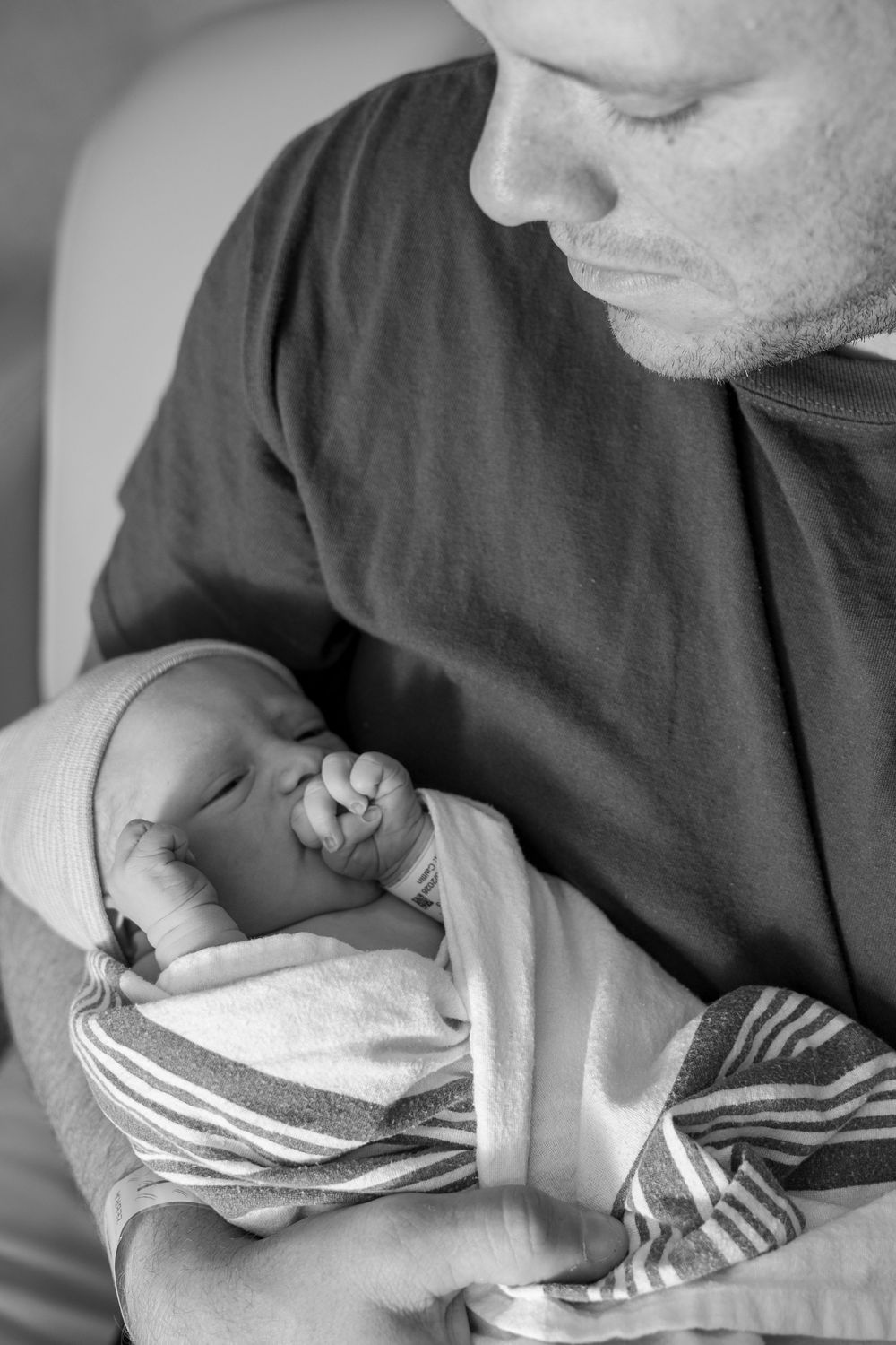 Black and white photo of a father tenderly holding his sleeping newborn baby wrapped in a striped blanket.