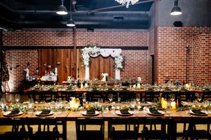 Elegant wedding reception in brick-walled venue with long banquet tables, floral arch backdrop, candlelight, and dark wood chairs Factory 51