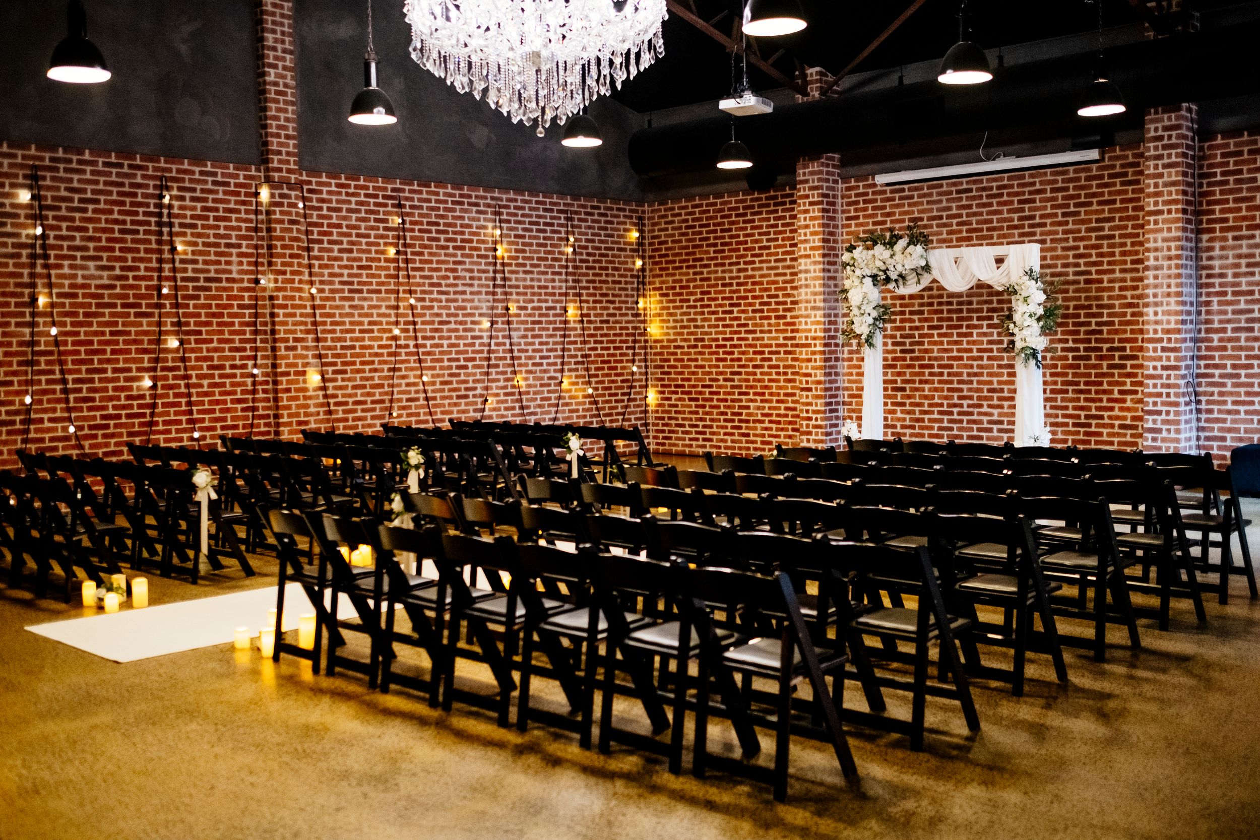 Elegant wedding venue with black chairs, brick walls, chandelier, and floral arch altar with string lights at Factory 51 Brisbane