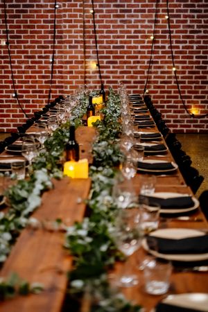 Elegant long wooden dining table with greenery runner, candles, and glassware against a brick wall at Factory 51 Brisbane