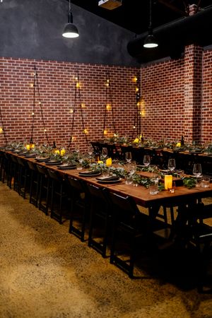 Rustic brick-walled private dining room with long wooden tables set for a banquet, adorned with greenery and candlelight Factory 51 Brisbane