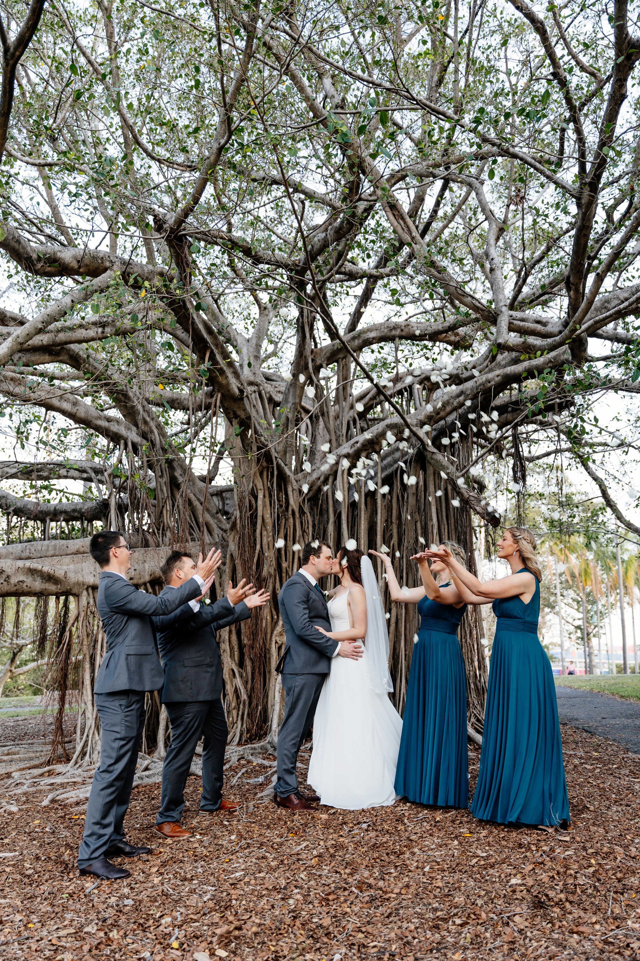 Wedding party celebrating under a banyan tree, bridesmaids in teal gowns and groomsmen in gray suits cheering the couple Factory 51 Brisbane