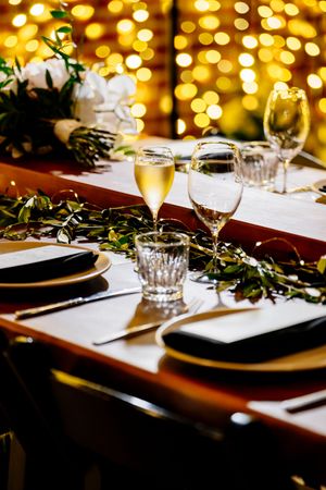 Elegant holiday table setting with champagne glasses, greenery, black plates, and warm golden bokeh lights in background at Factory 51