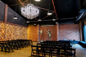 Elegant wedding venue with crystal chandelier, black chairs, brick walls, and floral arrangements in an industrial-chic space at Factory 51