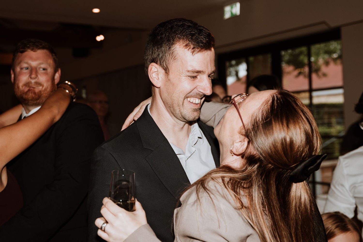Two people sharing a joyful embrace and laughing together at a lively indoor social event or party.