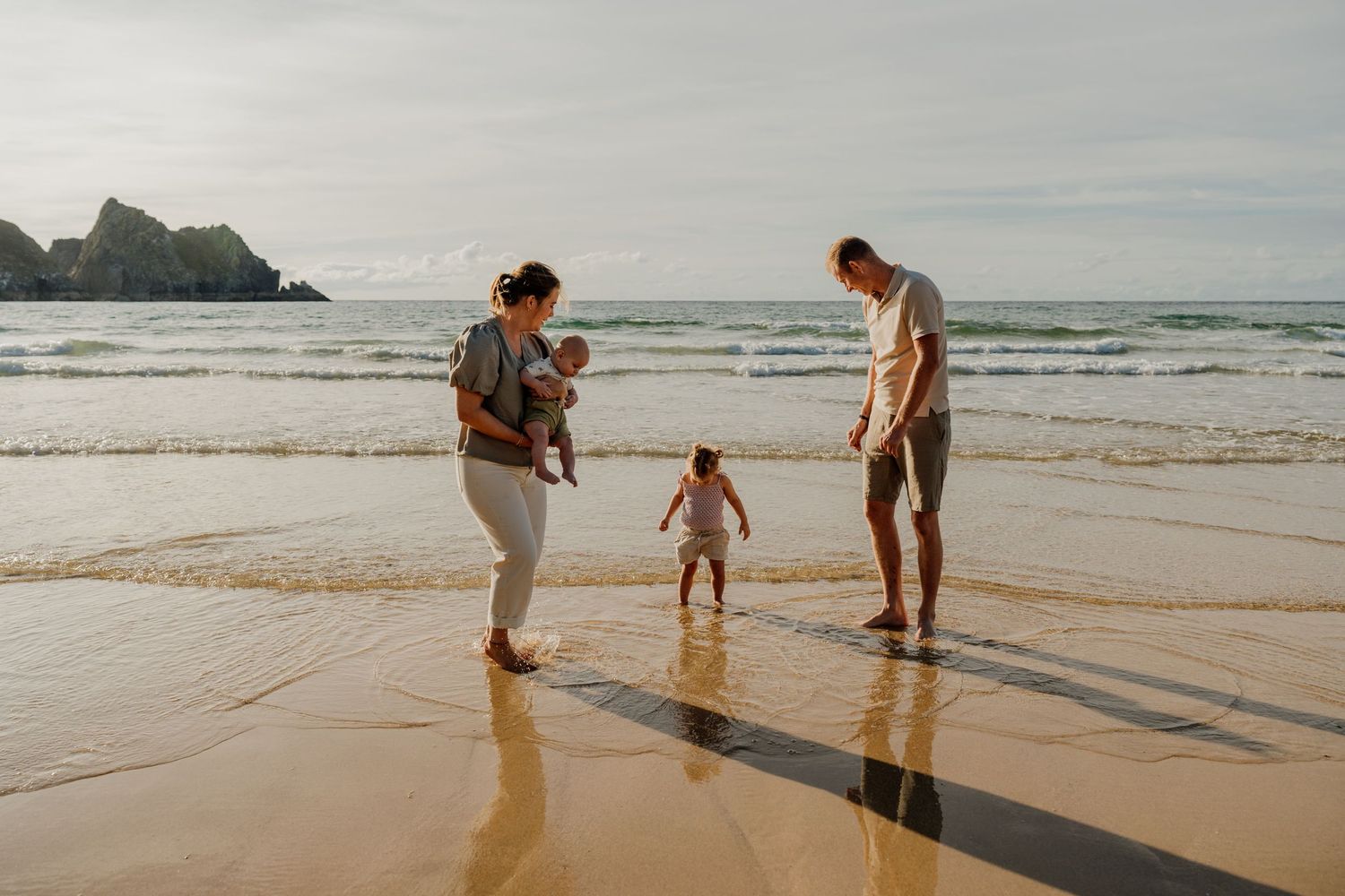 A young mother tenderly holds her smiling baby on a sunny beach, sharing a joyful moment together.