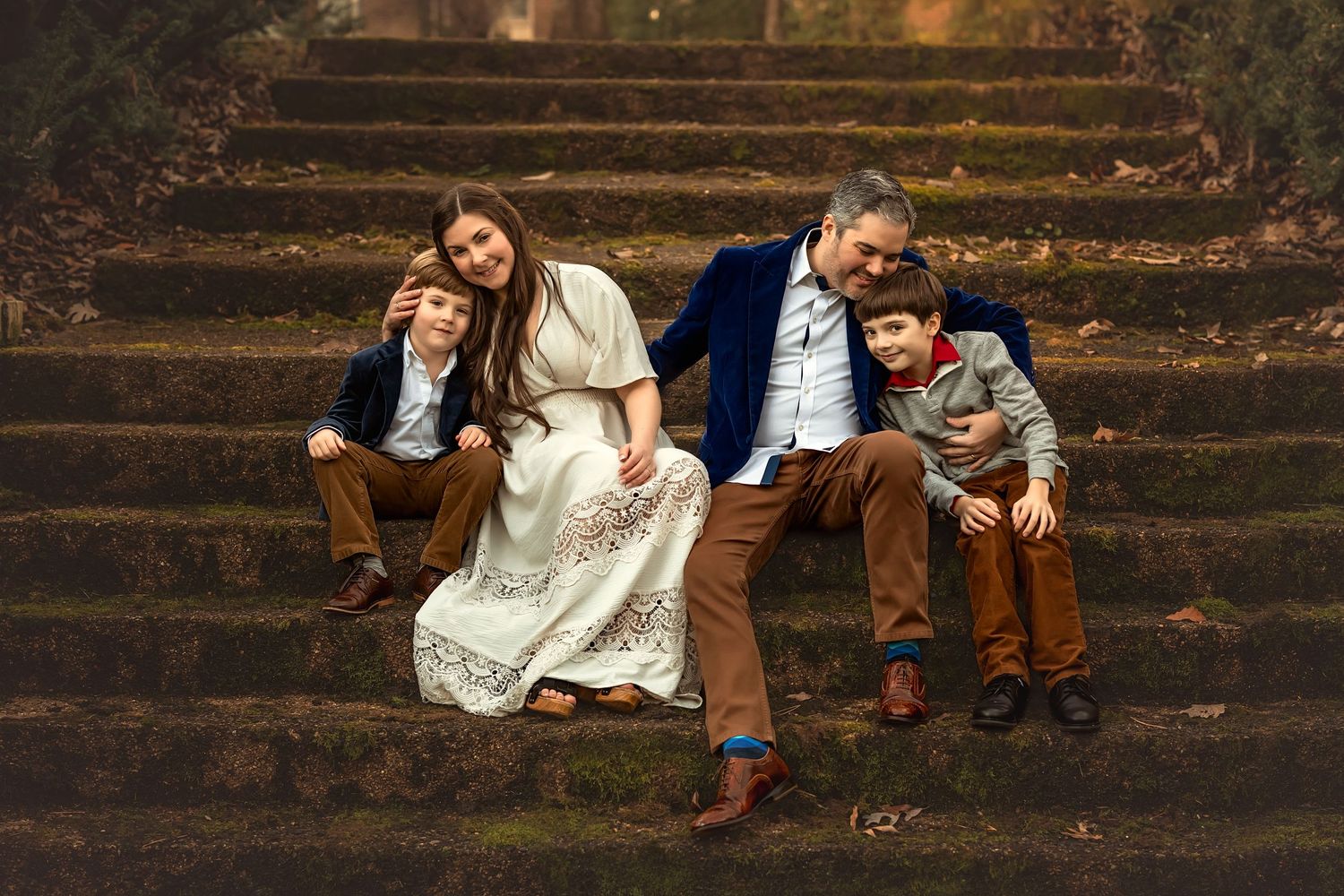 Family of four posing on stone steps in autumn, wearing coordinated earth tones and blue, smiling warmly together.