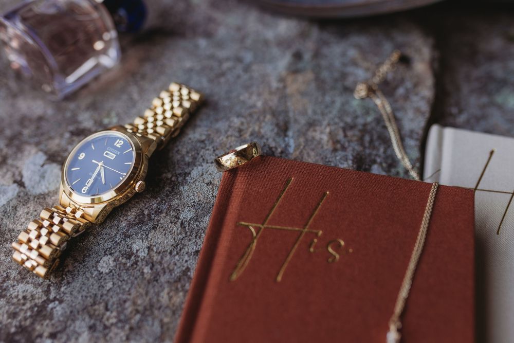 Gold watch, His vow book, necklace and cologne arranged as groom wedding day flat lay.