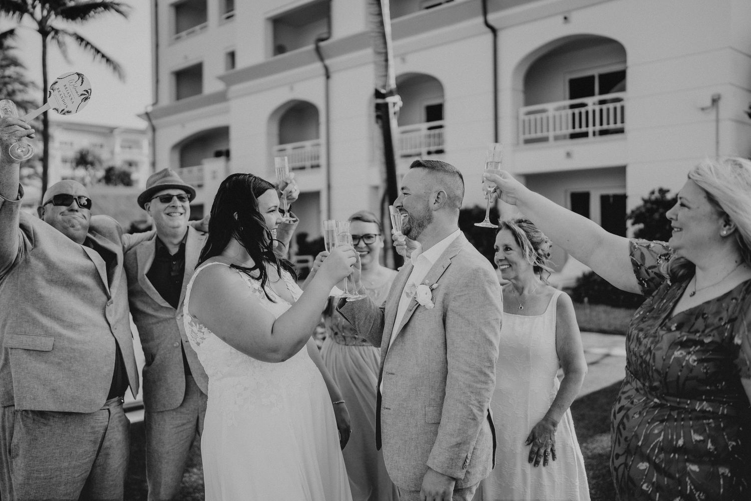 Bride and groom walk hand-in-hand along a tropical palm-lined path by a beachside resort on their wedding day.