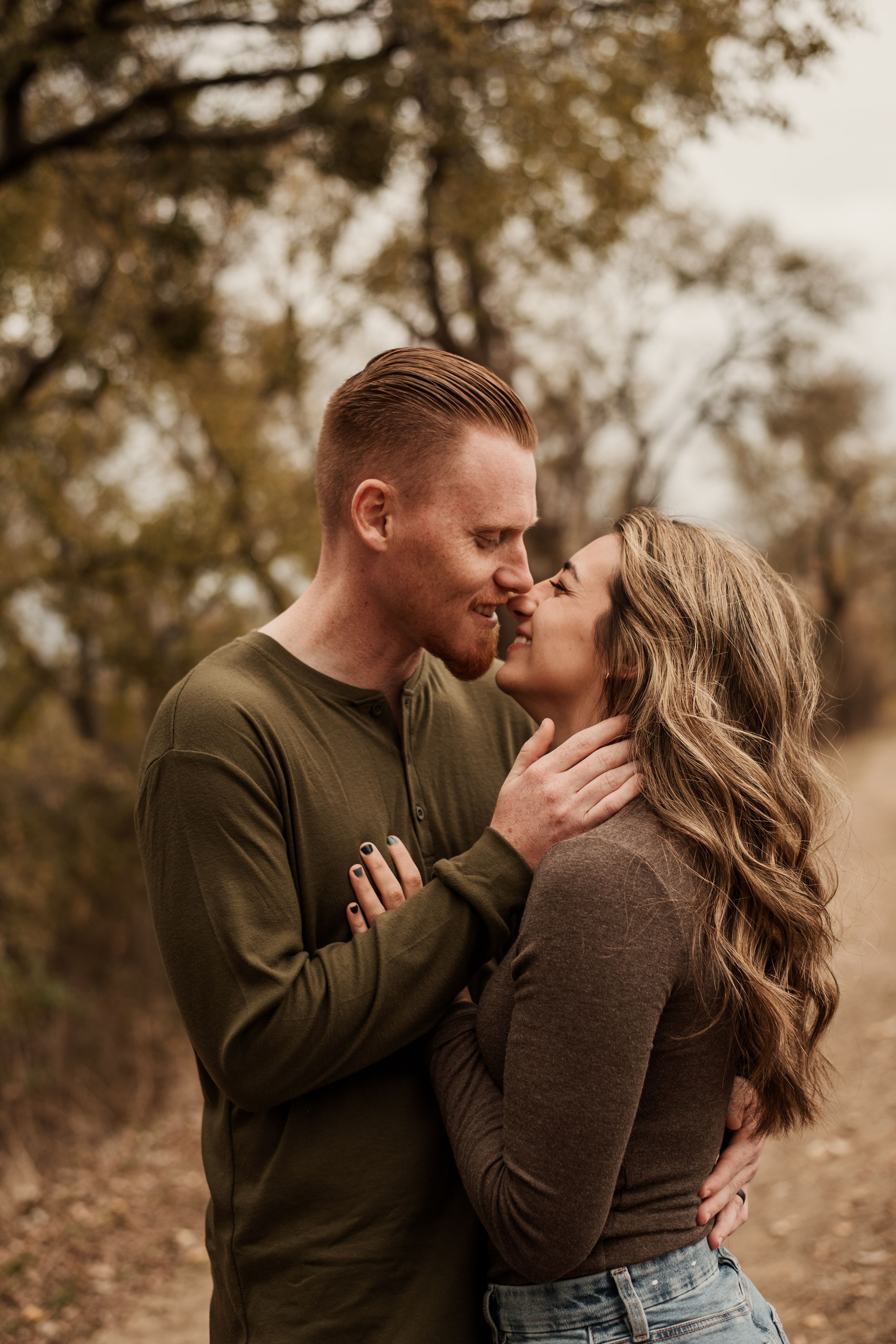Couple sharing a romantic almost-kiss moment outdoors in autumn, wearing coordinating olive and brown long-sleeve tops.