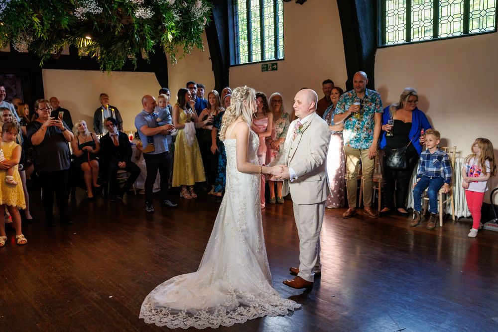 Bride and groom exchange vows at elegant indoor wedding ceremony with guests standing in rustic venue.