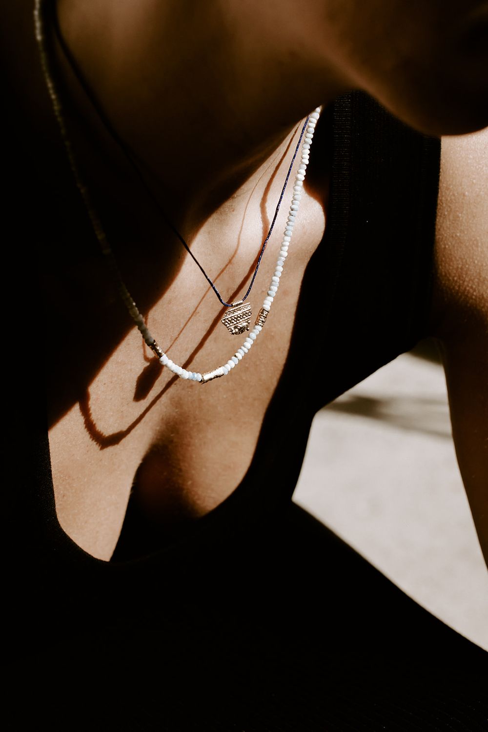 Layered beaded necklaces with a gold pendant on a woman wearing a black top in warm sunlight.
