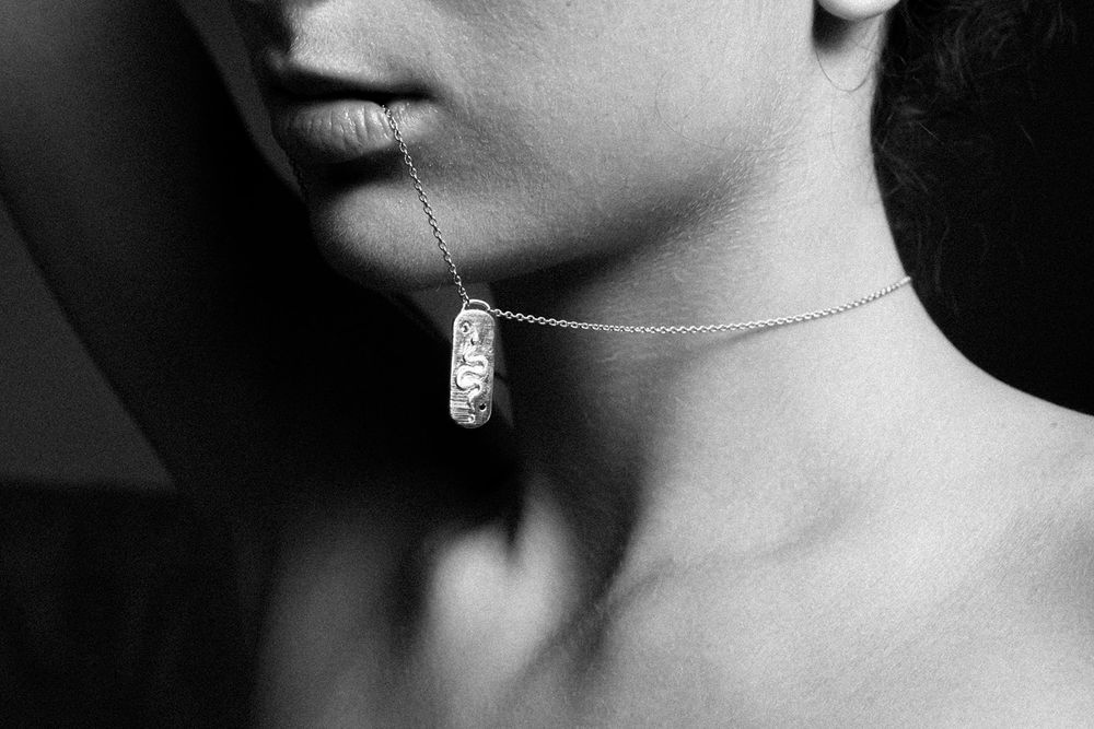 Black and white photo of a woman wearing a delicate silver chain necklace with a cylindrical pendant.