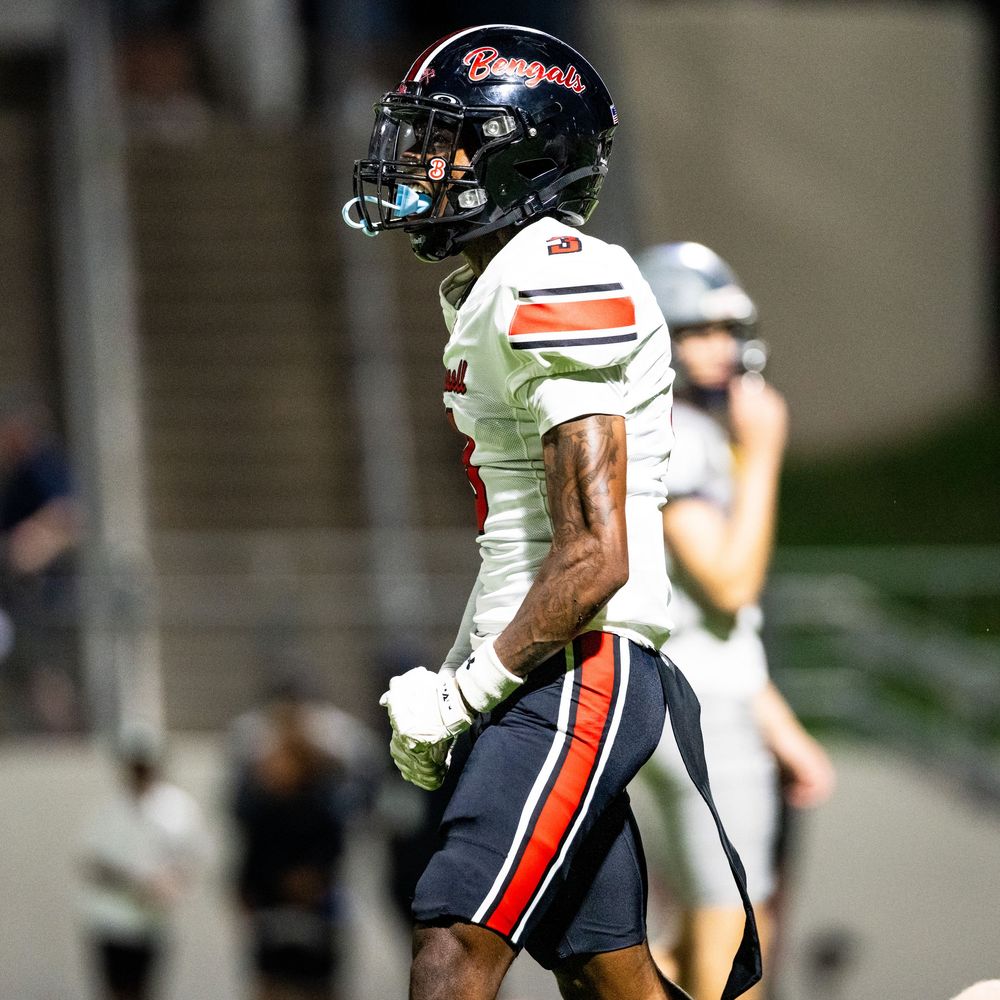 High school football player in Bengals team uniform celebrates on the field during a night game.