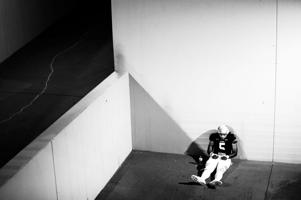 Lone football player sits against wall in black and white photo in a quiet stadium tunnel.