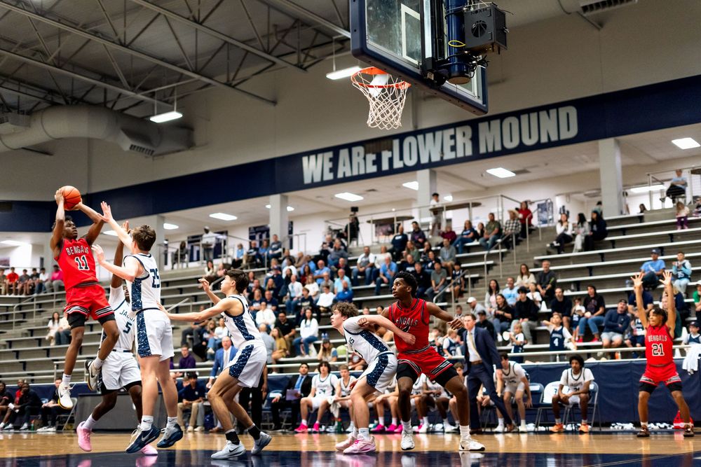 Basketball game in progress at Flower Mound high school gym with packed student crowd.
