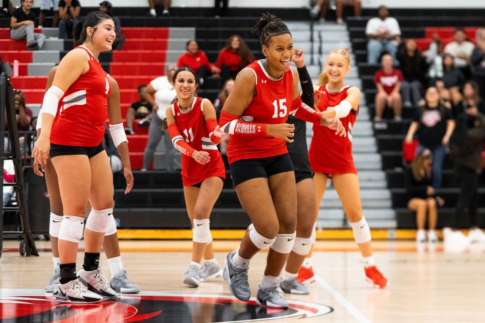 Volleyball player number 15 in red uniform celebrates a point with teammates on court.