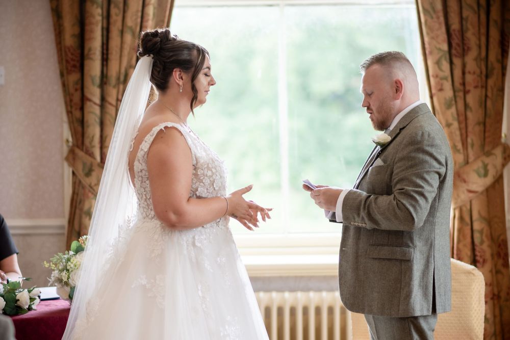 Bride and groom exchanging wedding vows during an intimate ceremony in an elegant room with curtained windows.