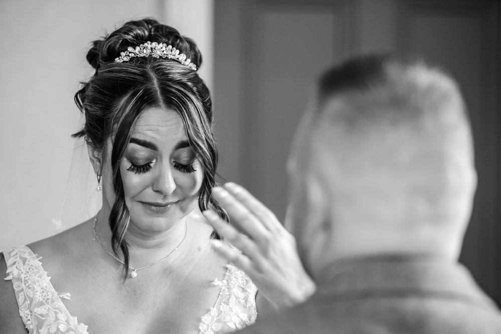 Black and white photo of an emotional bride crying as a man gently wipes her tears on her wedding day.