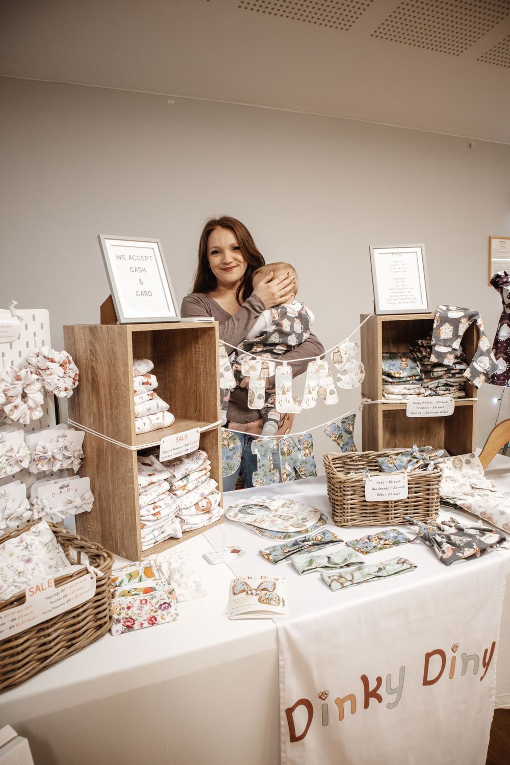 Woman smiling behind a craft market stall displaying baby products for Dinky Diny brand.