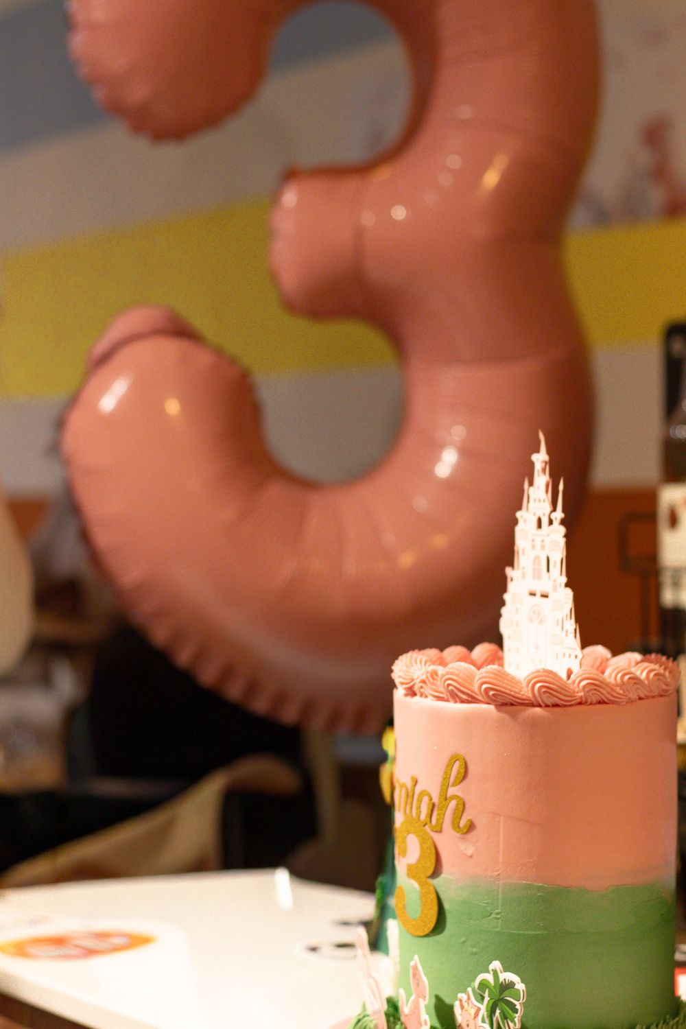 Pink 3rd birthday cake with castle topper and number 3 balloon in background.