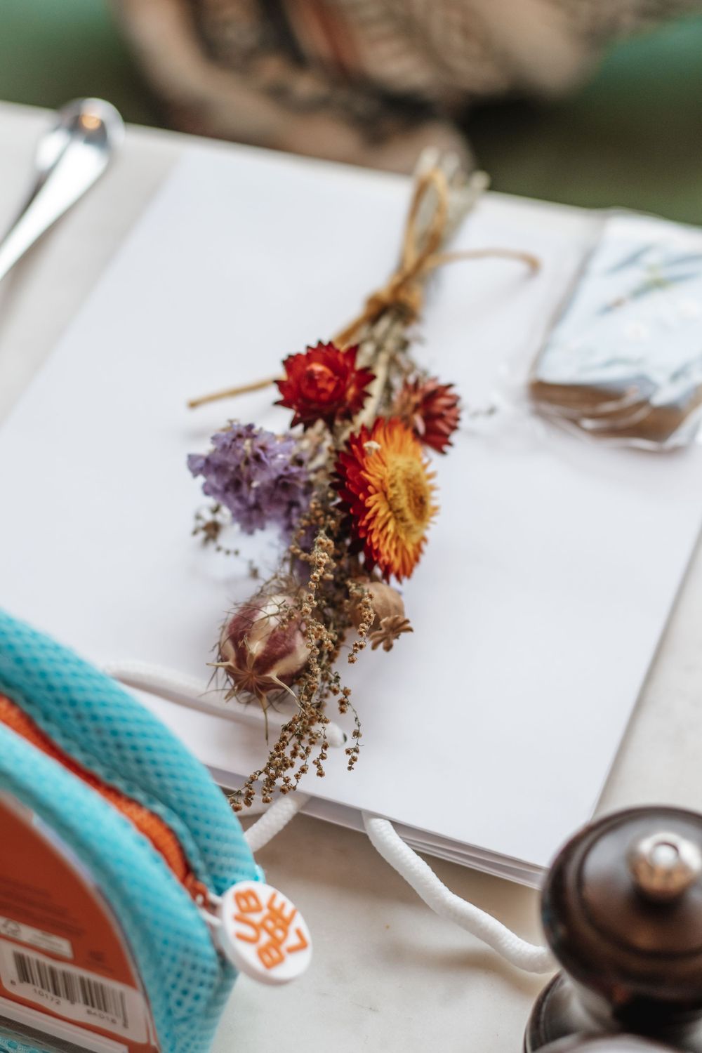 Dried wildflower bouquet tied with twine resting on an open white notebook on a marble table.