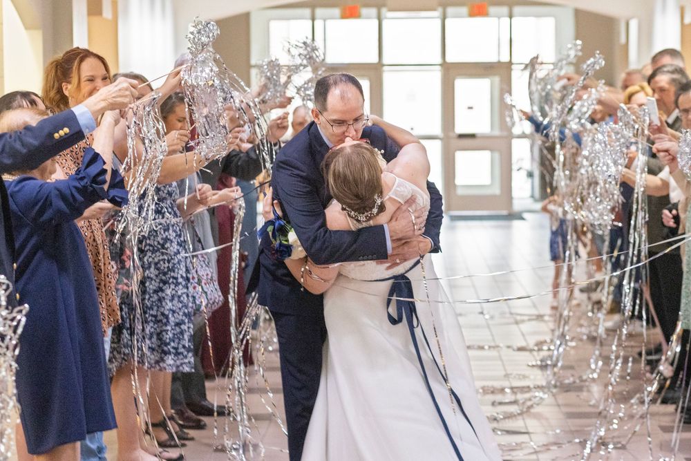 Bride and groom share a joyful hug during their wedding send-off with guests waving silver wands.
