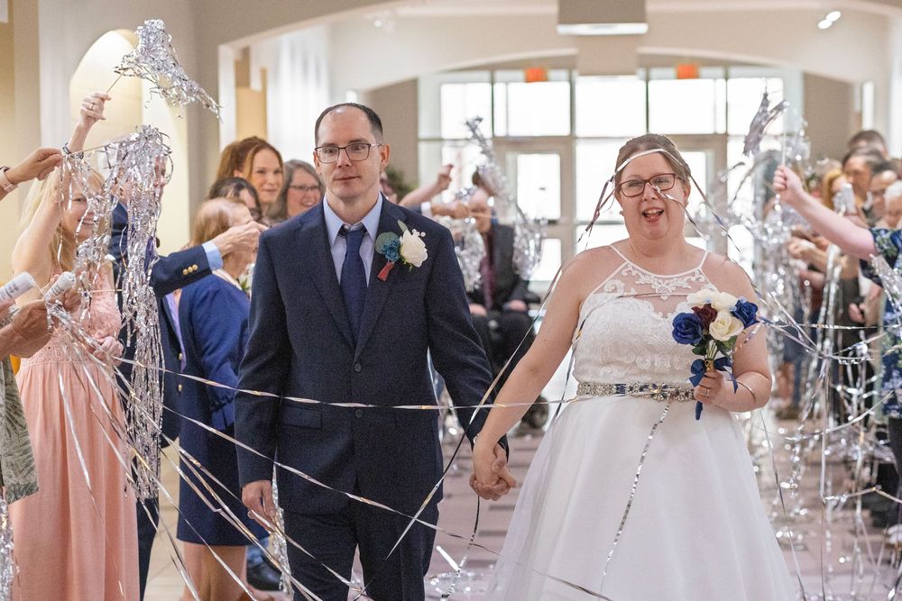 Bride and groom walk hand-in-hand through a festive streamer send-off during their wedding reception celebration.