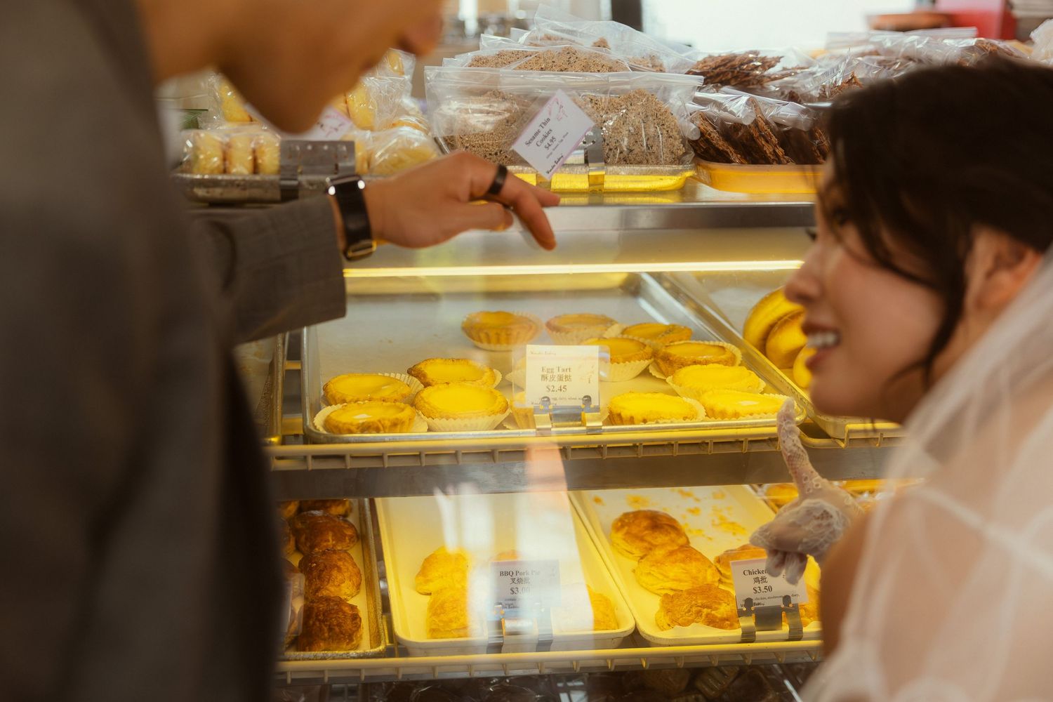 Two people selecting pastries from a bakery display case filled with golden croissants and baked goods.