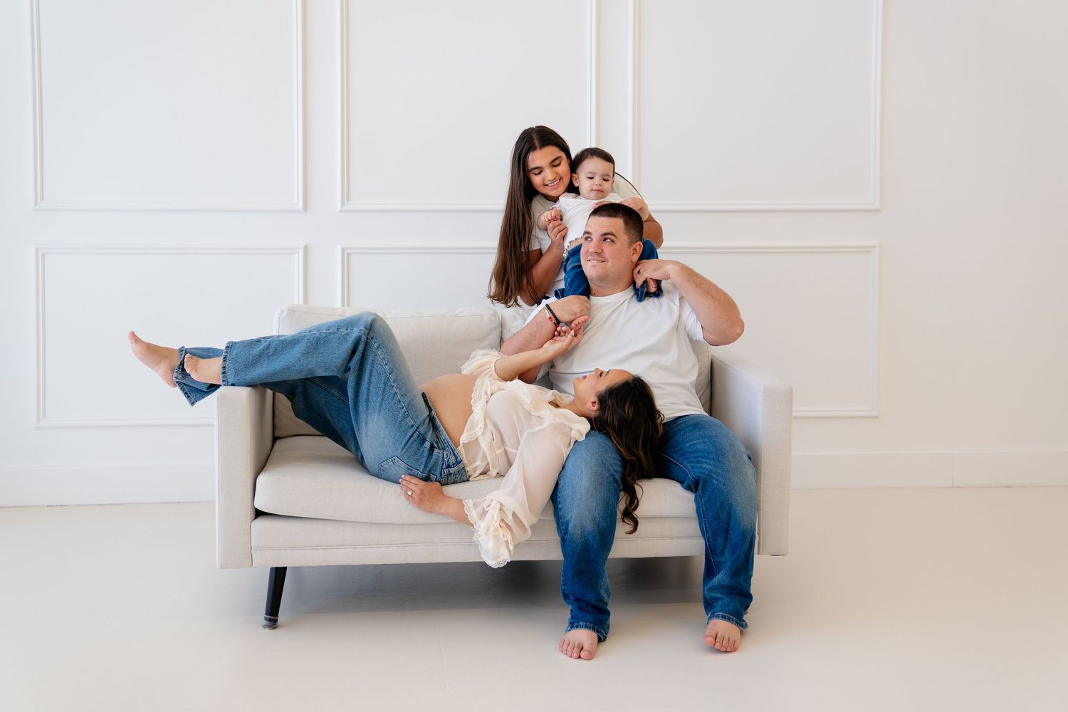 Happy family of four relaxing together on a white sofa in a bright, modern living room, smiling and bonding.