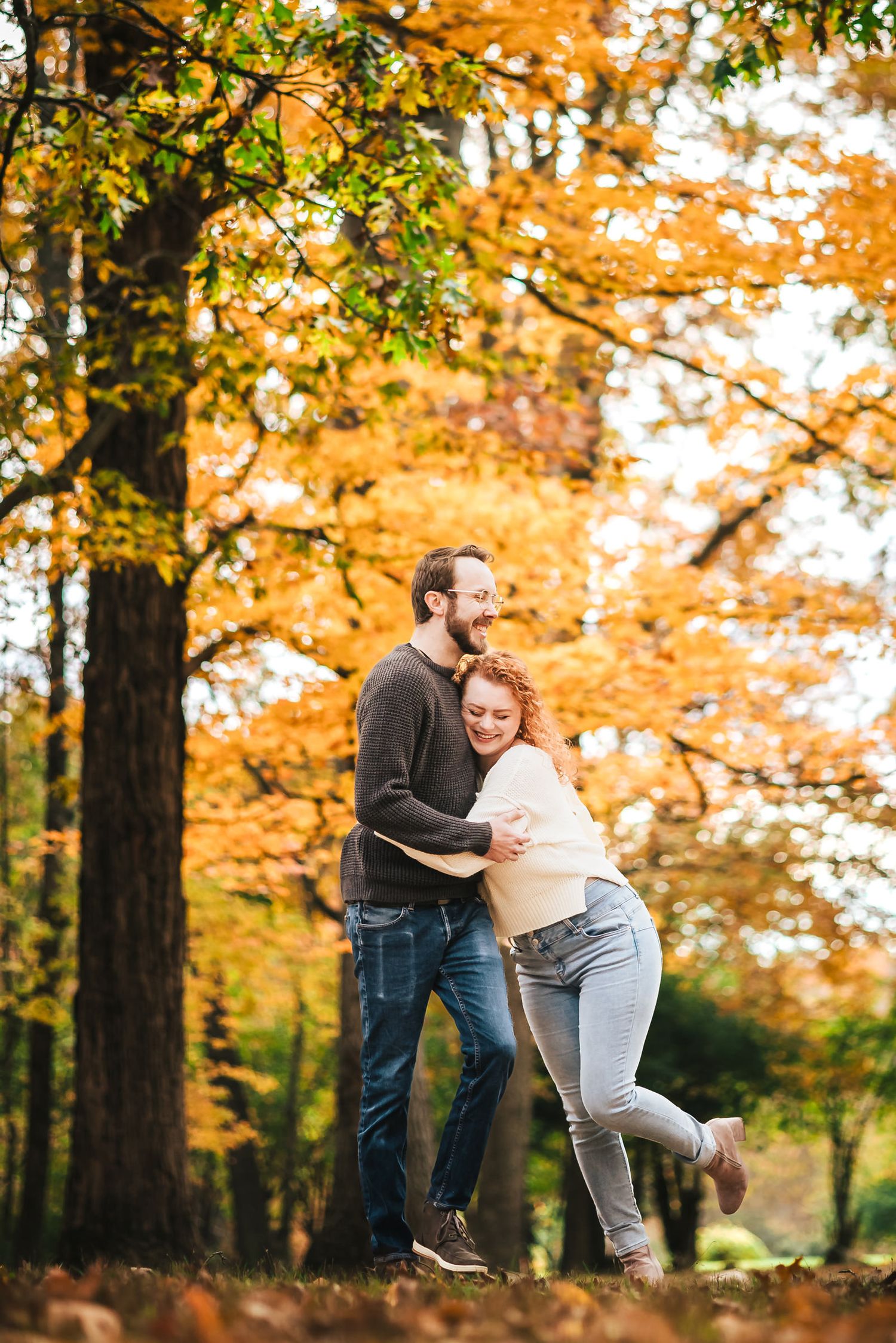 Engaged couple embracing and laughing on a trail at Borderland State Park, her leg kicked up mid-laugh.