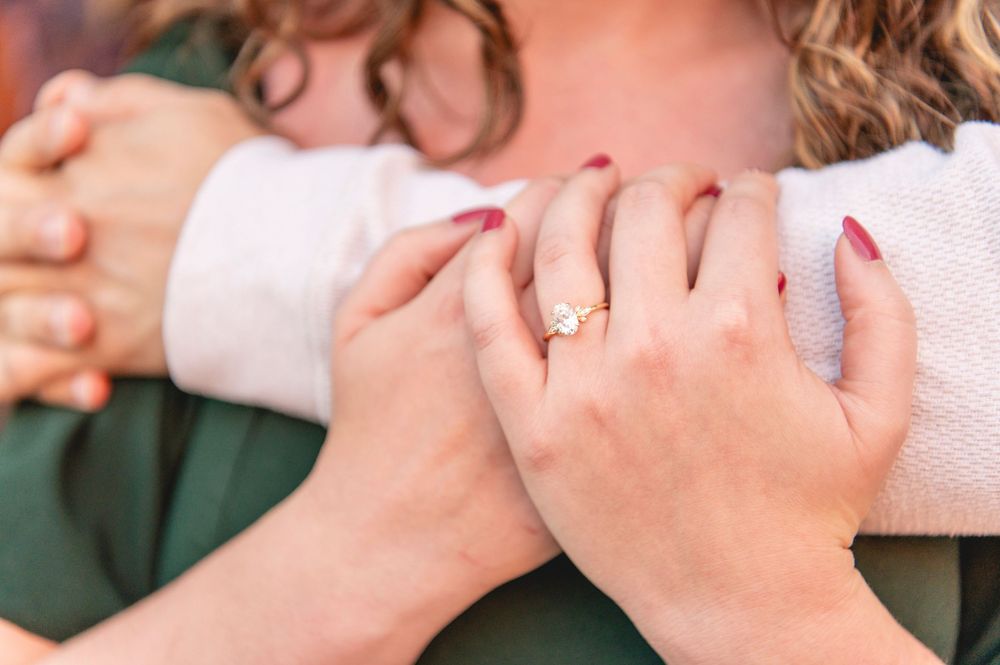 Close-up of two people embracing, one wearing a gold diamond engagement ring with red manicured nails.