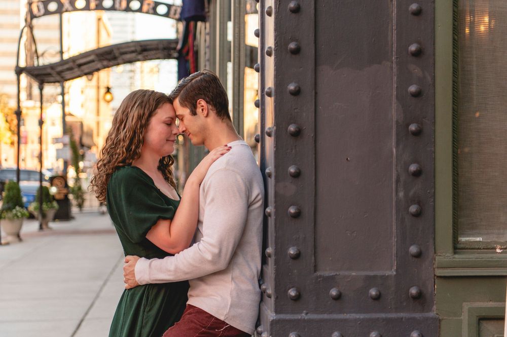 Couple sharing a romantic moment leaning against a green metal pillar on a city sidewalk during golden hour.
