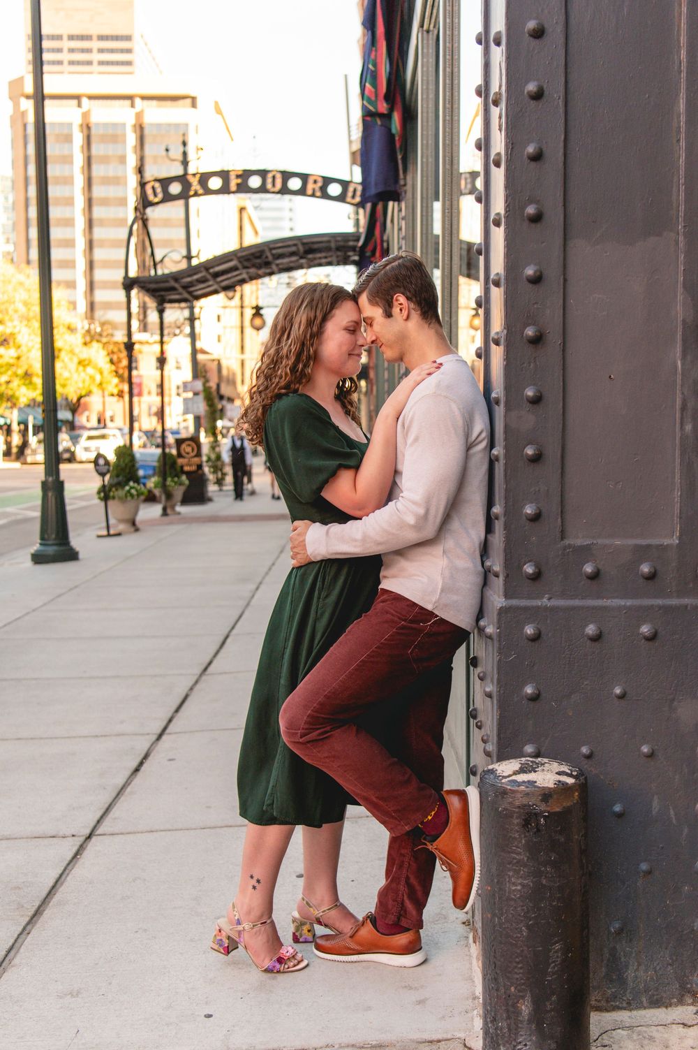Couple sharing a romantic moment leaning against a urban building wall on a sunny city sidewalk.