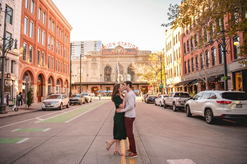 Couple embracing and kissing on a street in front of Union Station in Denver, Colorado at golden hour.