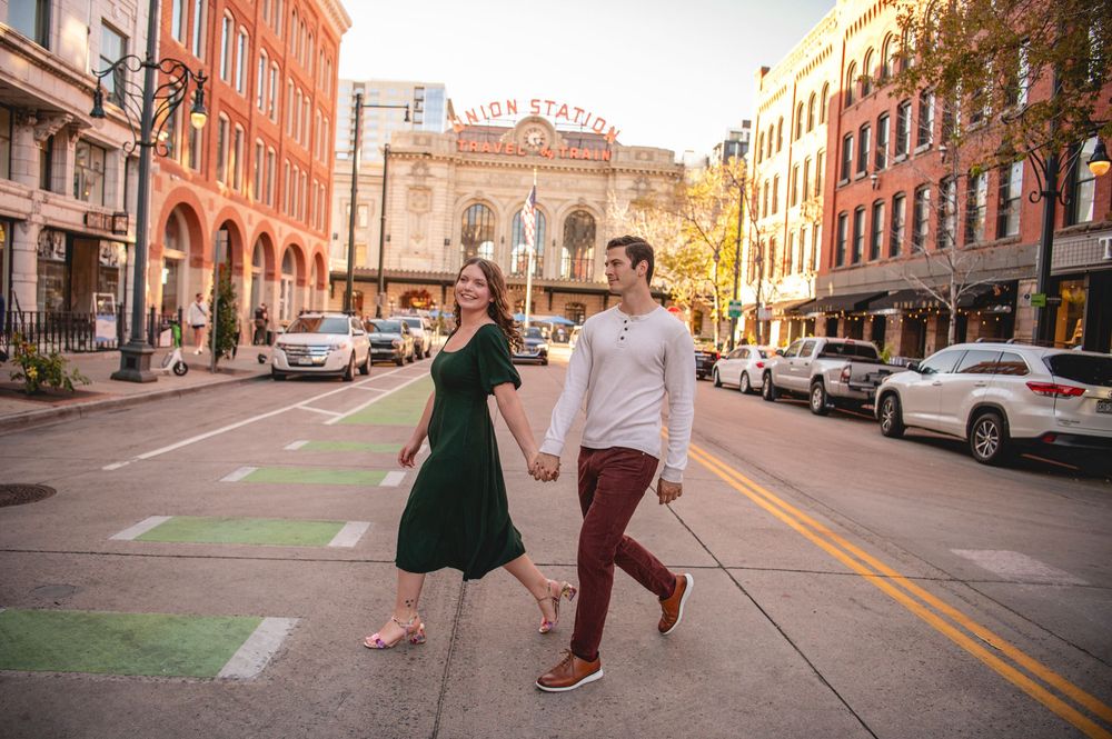 Couple holding hands crossing a sunny urban street in Nashville, woman in green dress, man in white sweater and burgundy pants.