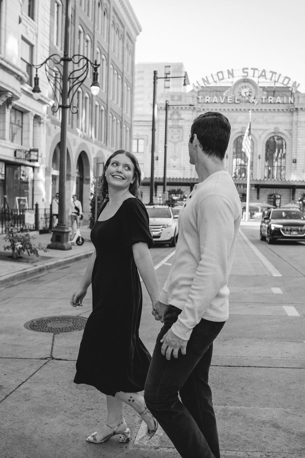 Couple holding hands walking near Union Station in black and white engagement photo.