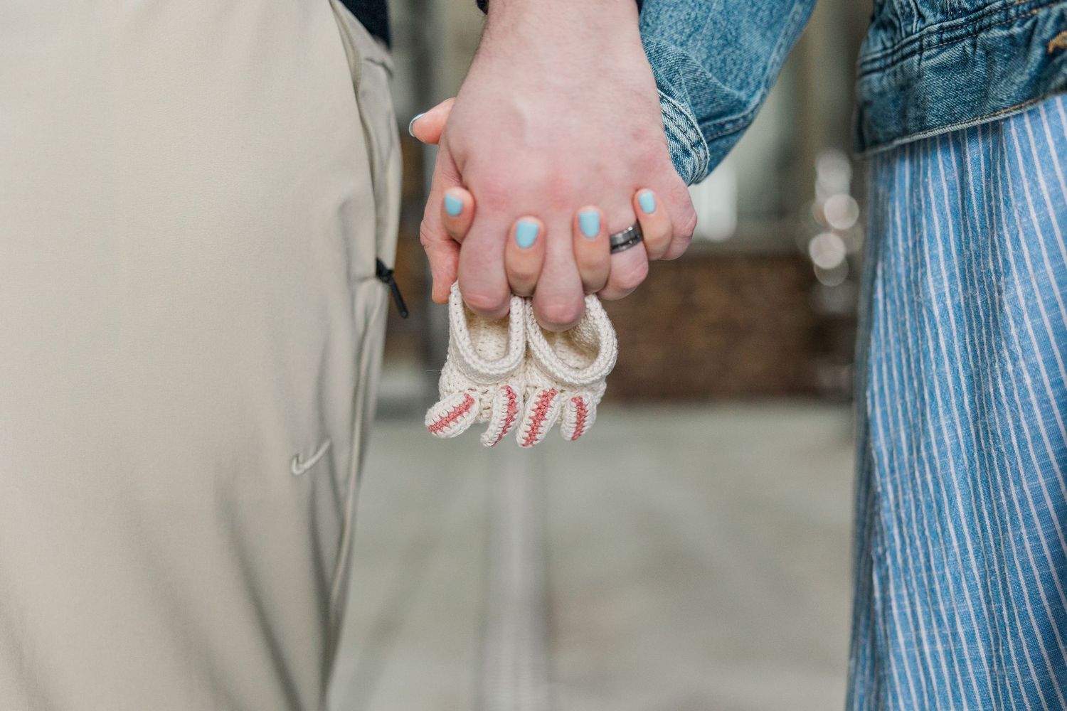 Couple holding hands with blue nail polish, sharing a decorative macrame keychain outdoors.