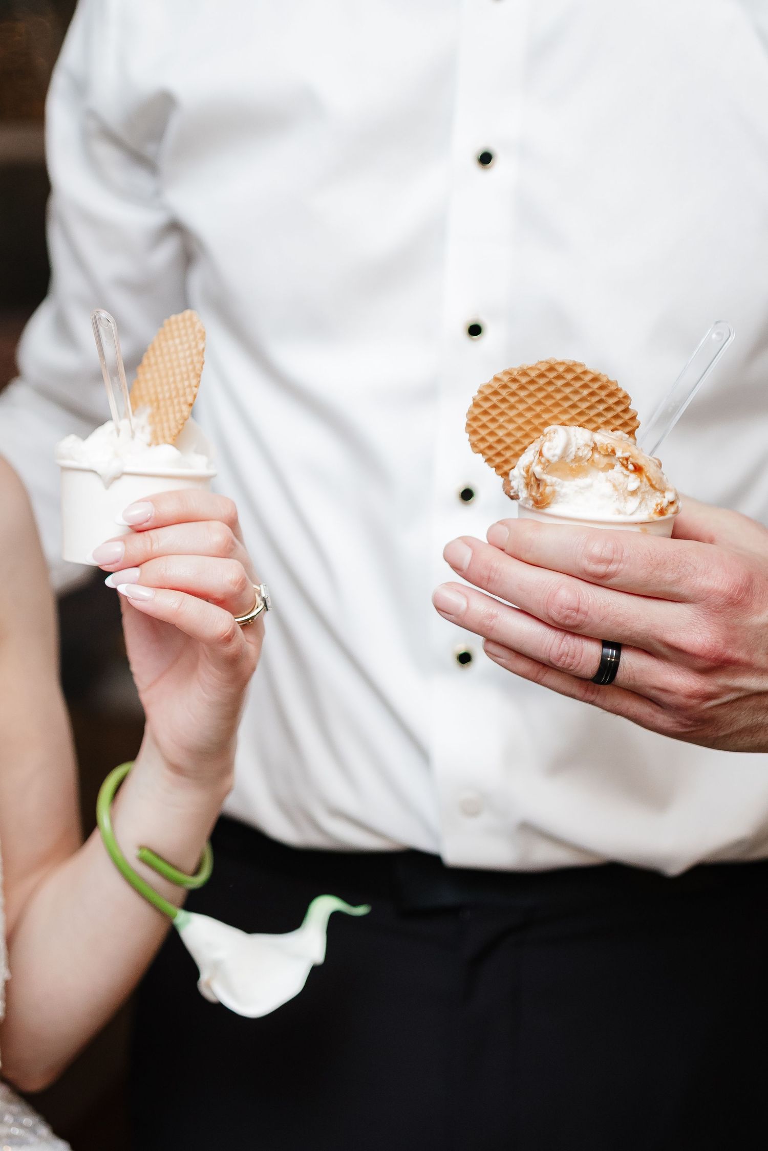 Bride and groom holding gelato cups with waffle cookies at a wedding reception dessert station.