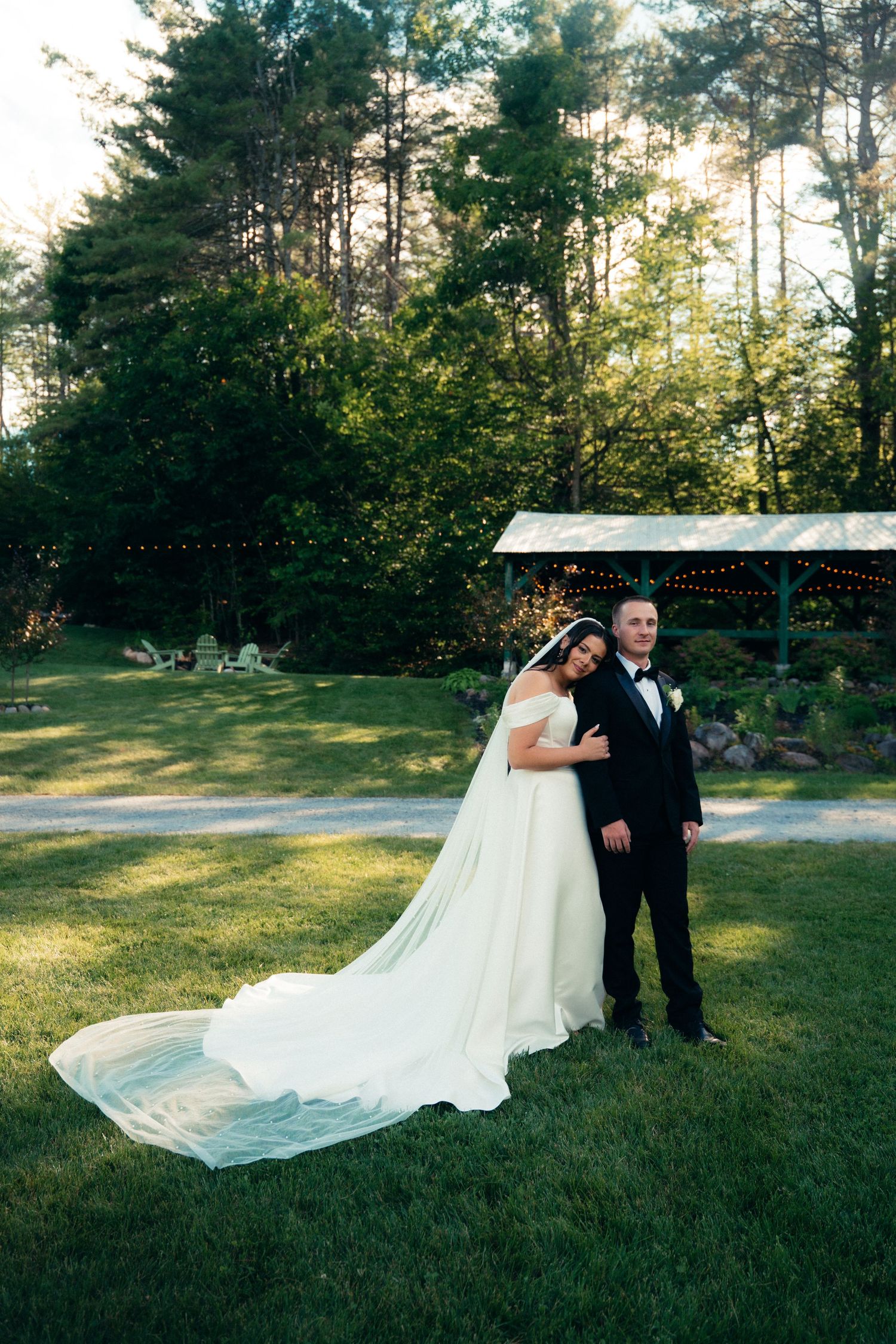 Bride leaning on grooms shoulder in a lush green outdoor garden setting at golden hour.