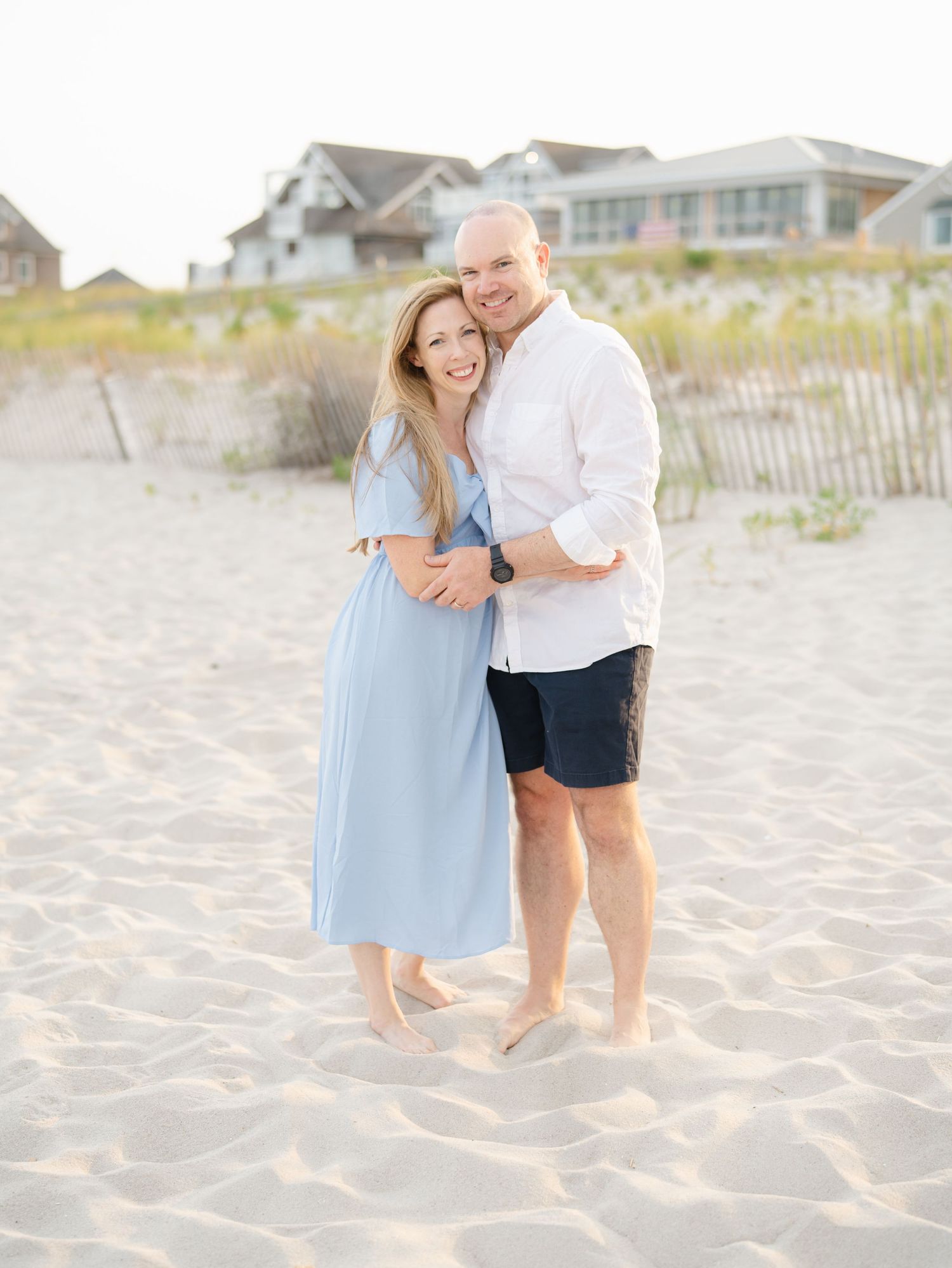 Mom and dad snuggle together on the beach while their children play.