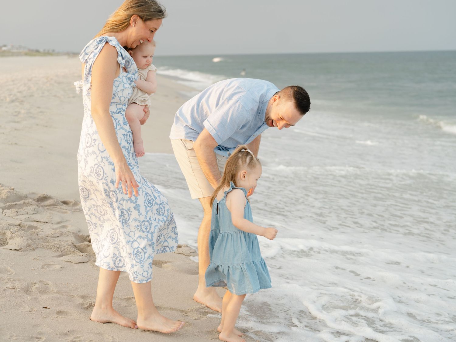 Young family walking barefoot along the ocean tide during golden hour in Mantoloking, NJ.