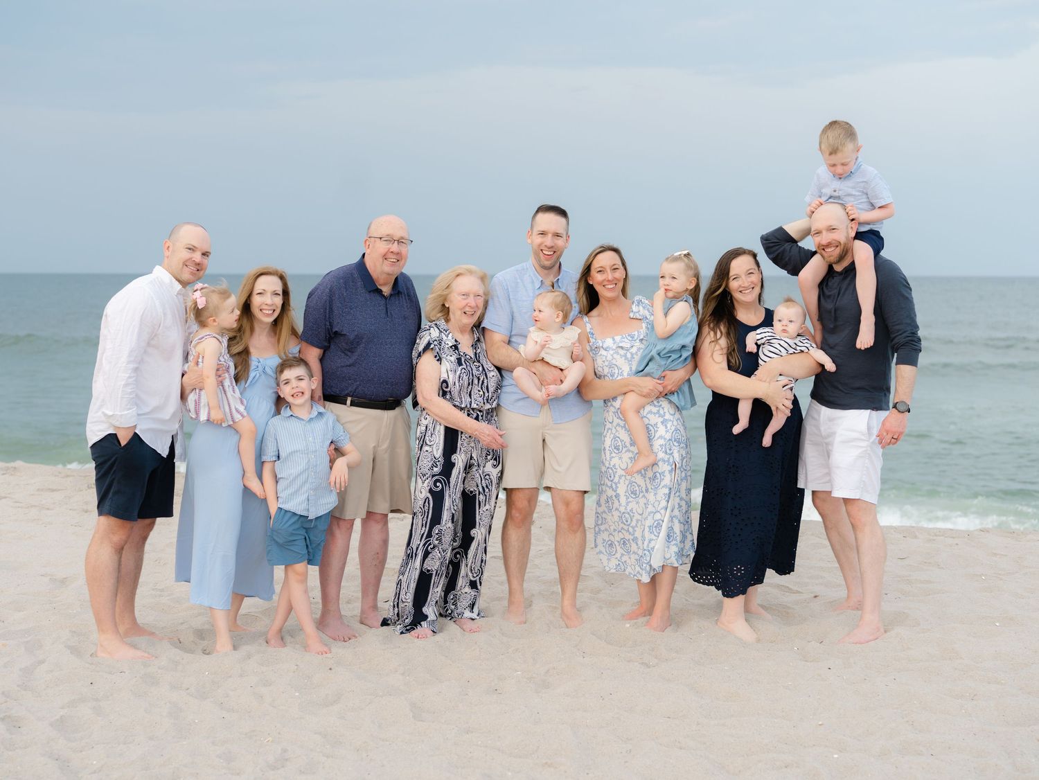 Three generations of family standing near the on the beach at the jersey shore while lauren marie photography photographs them.
