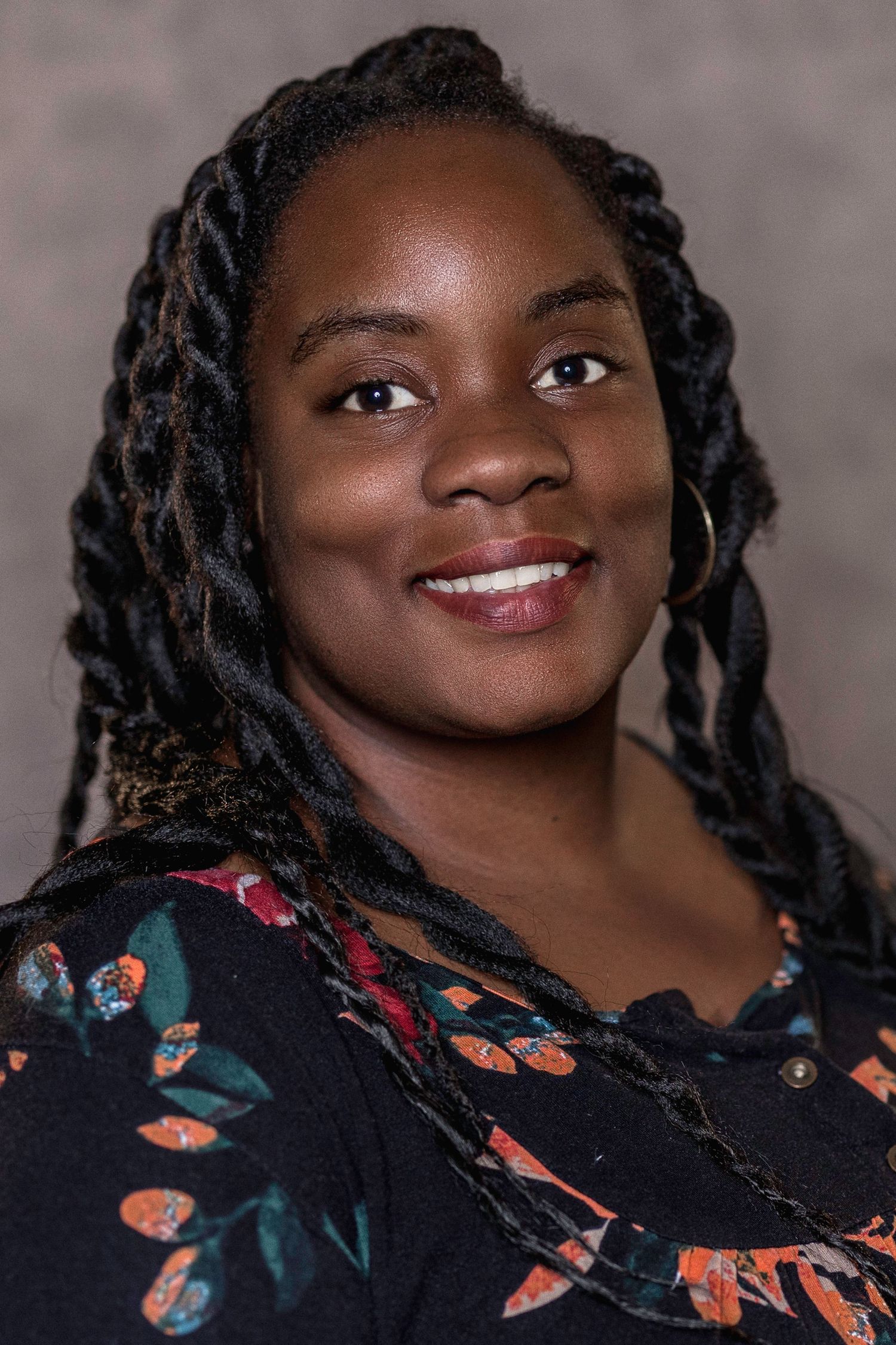 Young Black woman with braided hair smiling in floral top against neutral background.