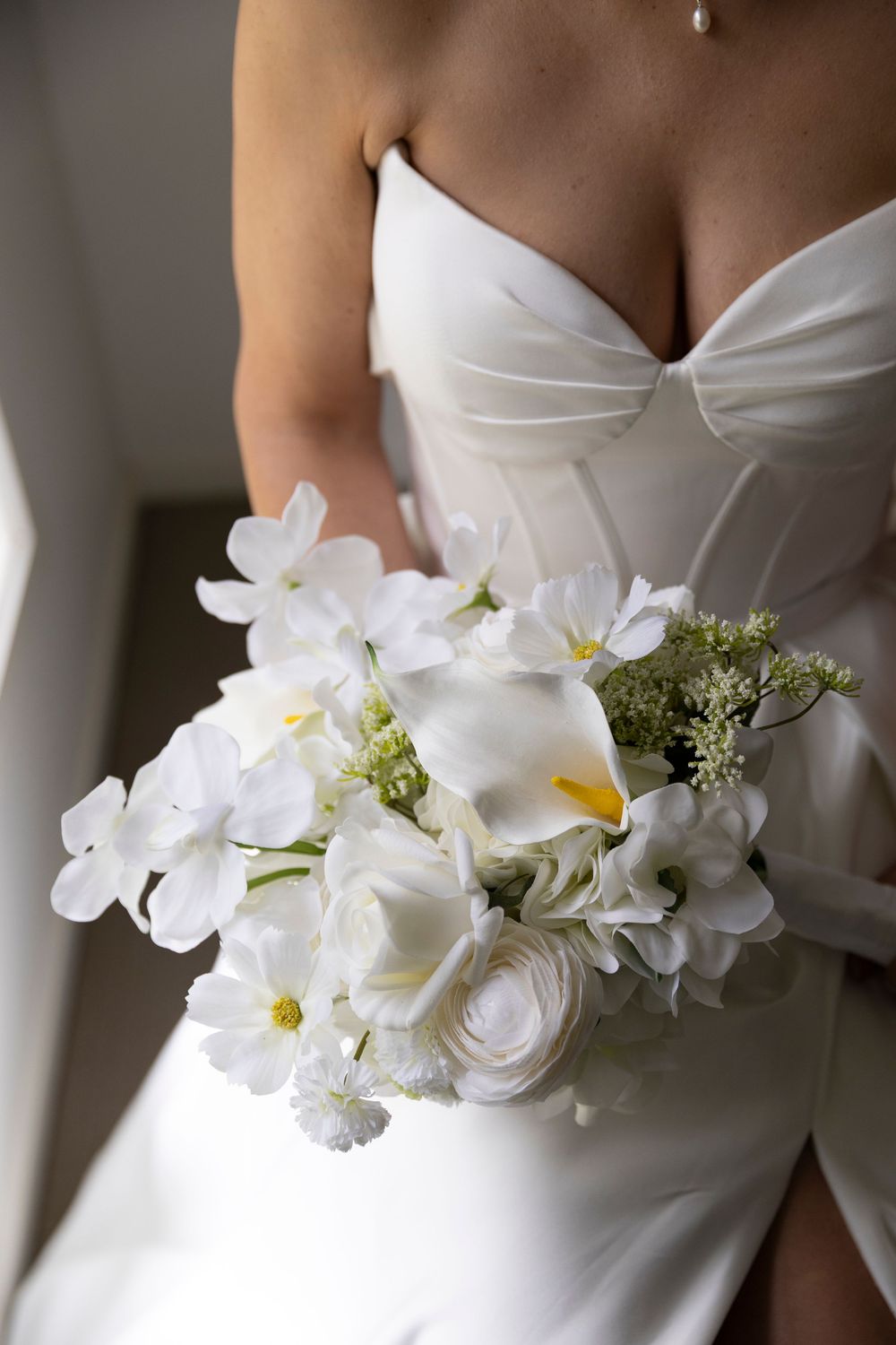 Bride in white strapless wedding gown holding elegant all-white bouquet with calla lilies, ranunculus, and orchids.