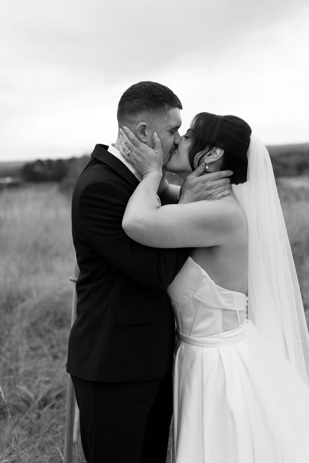 Black and white photo of bride and groom sharing a passionate kiss in an open field.