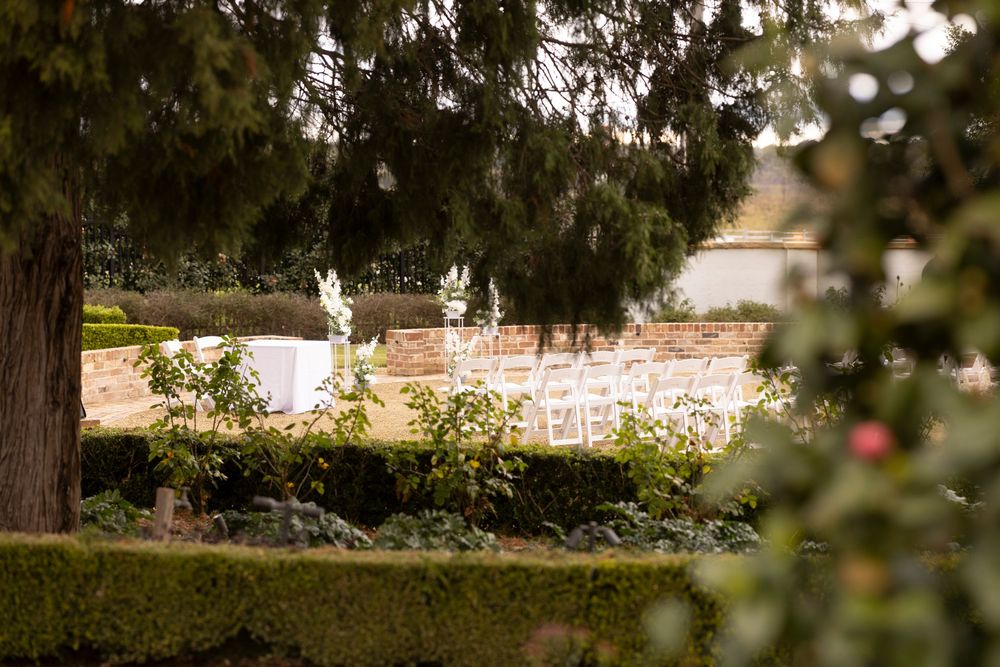 Elegant outdoor wedding ceremony setup with white chairs and floral arrangements in a lush garden setting.