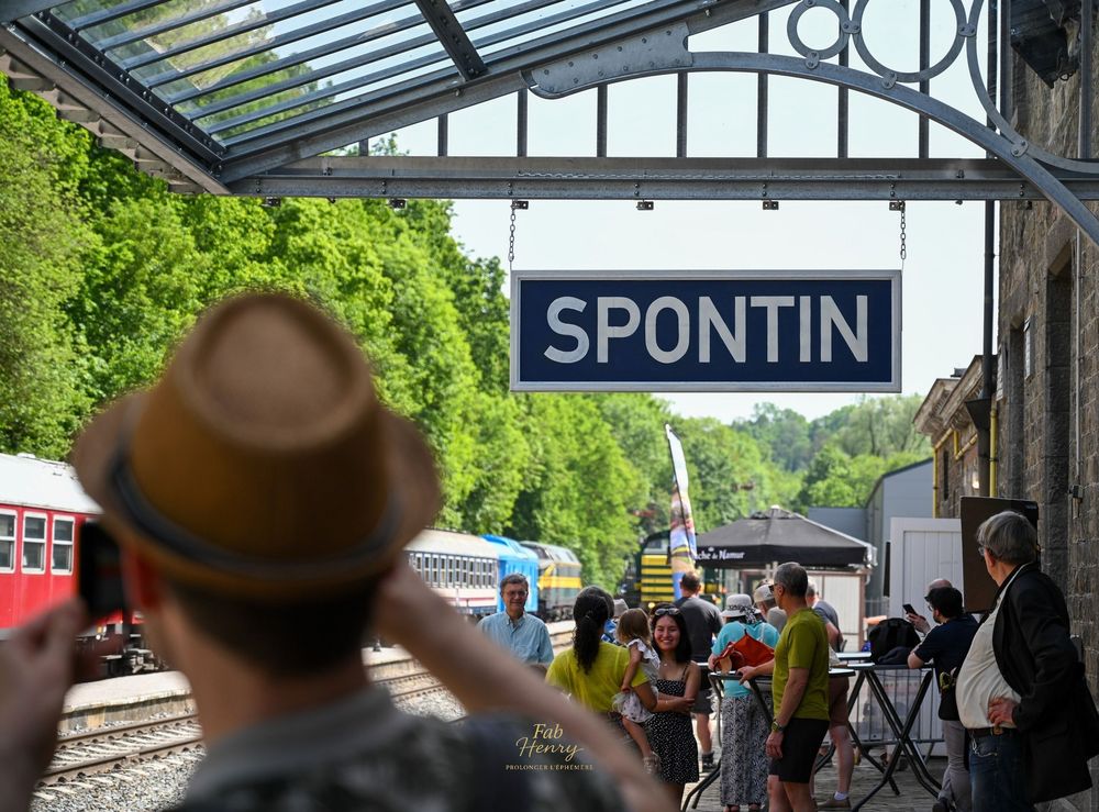 Personne au chapeau devant le panneau gare "SPONTIN", foule